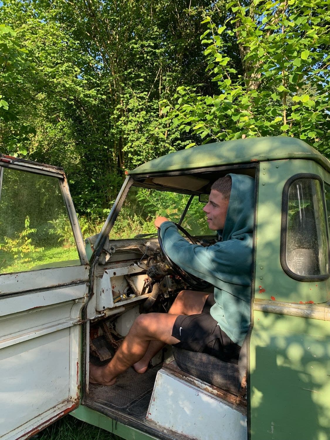 Un chico descalzo al volante de un todoterreno viejo en medio del bosque