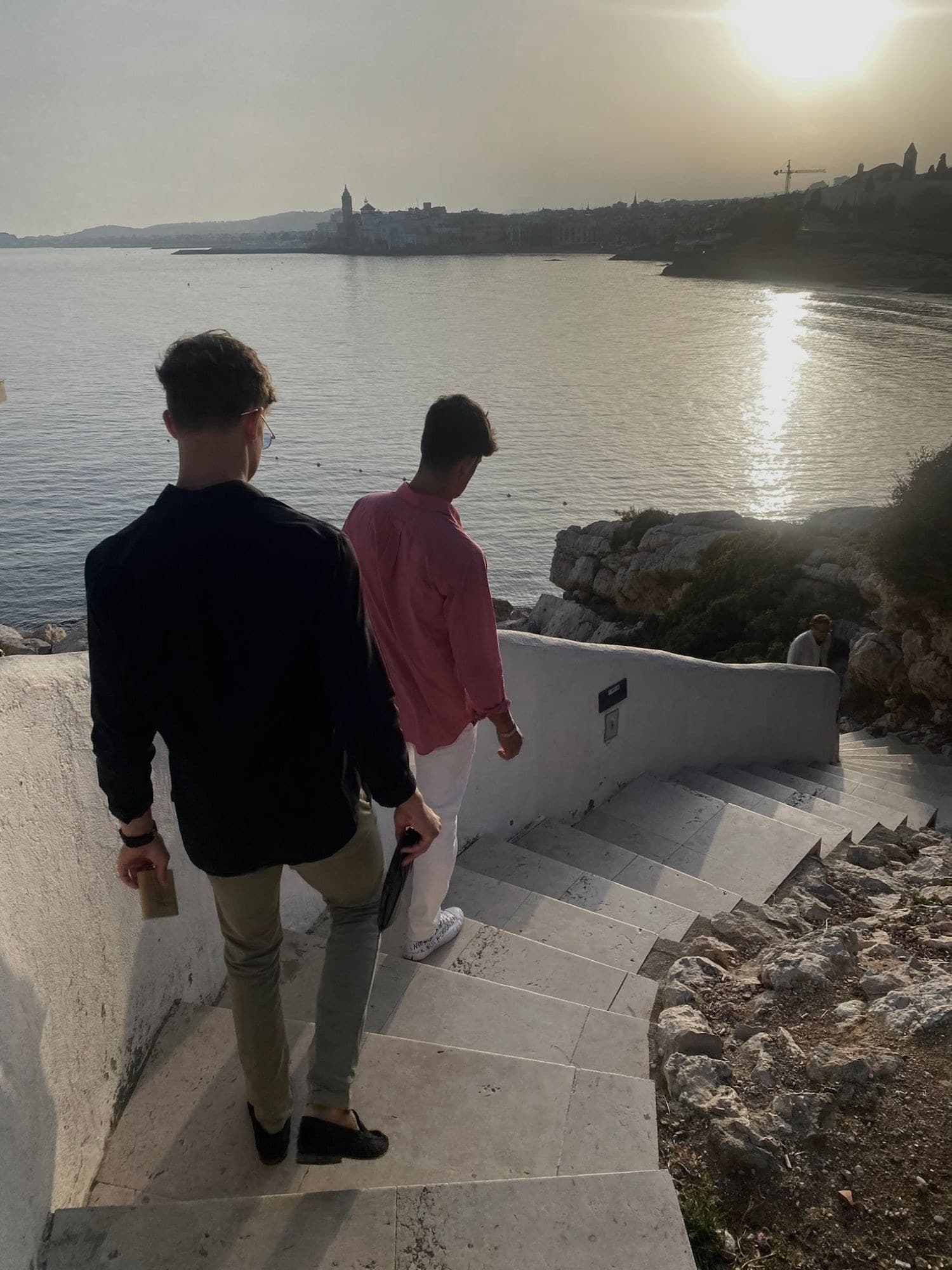Dos chicos bajando unas escaleras hacia el mar al atardecer